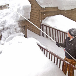 Man removing snow from a garage roof with rake.